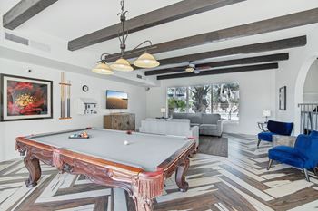 A pool table is in the middle of a room with a blue chair to the right. at The Viridian Apartments, Scottsdale